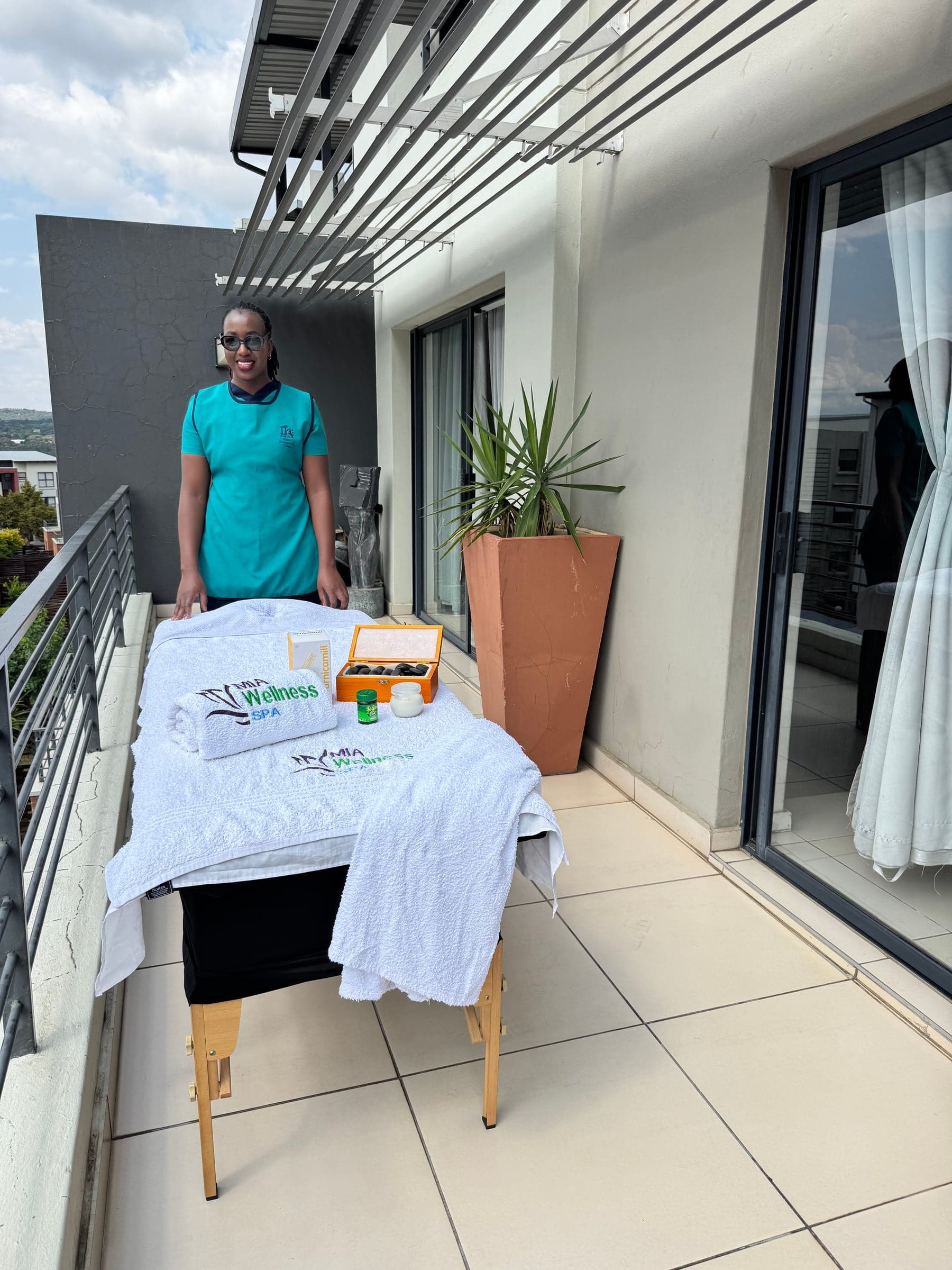 Mia Wellness Spa therapist standing beside a prepared treatment table on a balcony during a house-call massage setup.