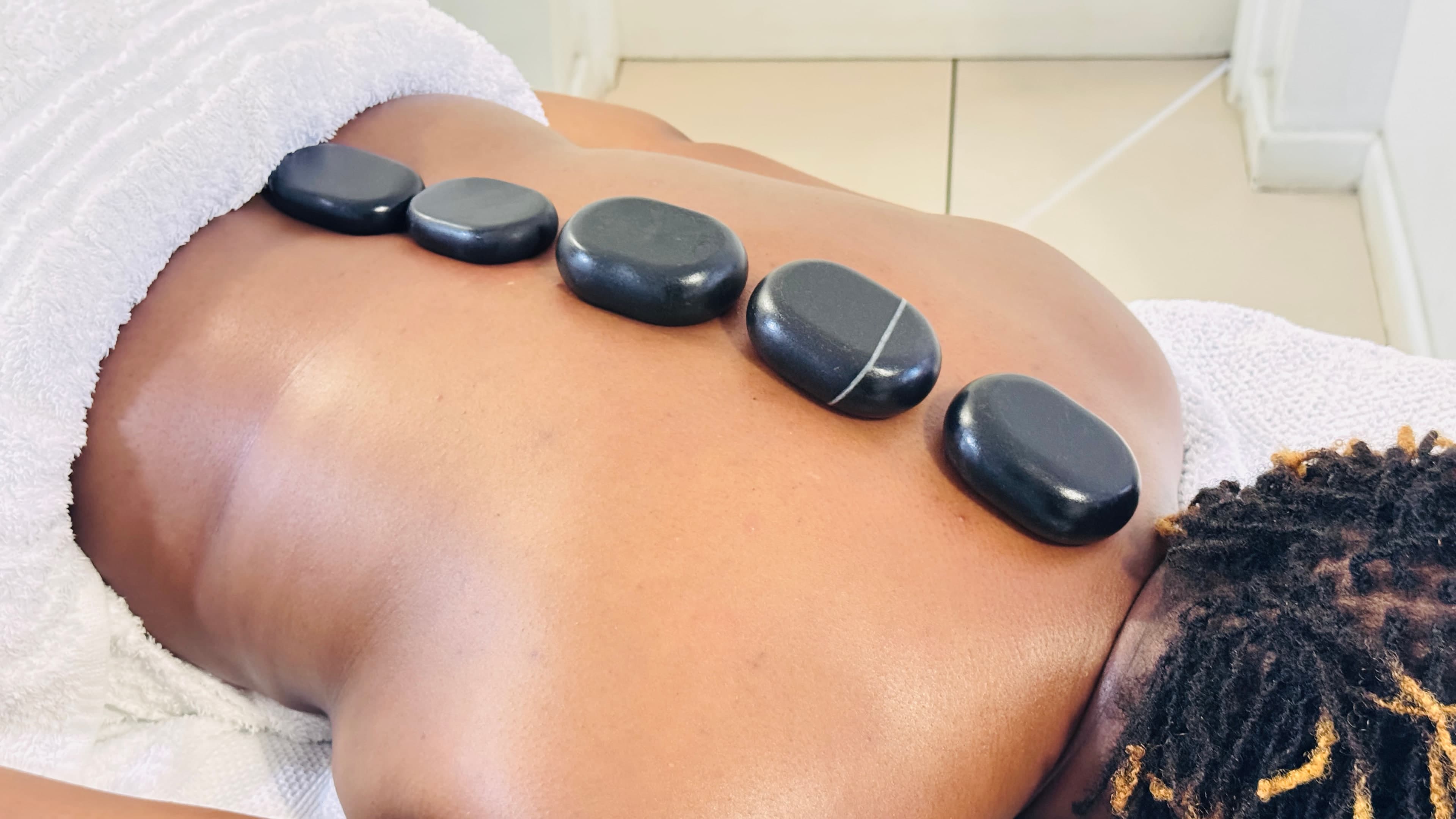 A client resting with heated stones placed along the back during a Mia Wellness Spa hot stone massage at home.